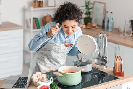 Young woman tasting dish in kitchenの写真素材