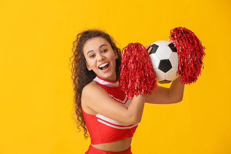 Beautiful young cheerleader with soccer ball on color backgroundの写真素材