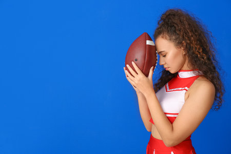 Beautiful young cheerleader with ball on color backgroundの写真素材
