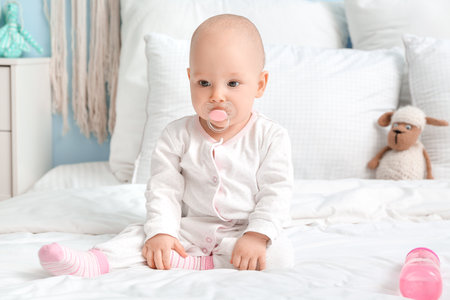 Cute little baby with bottle of water on bed in room