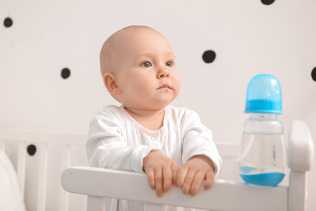 Cute little baby with bottle of water in crib at homeの写真素材