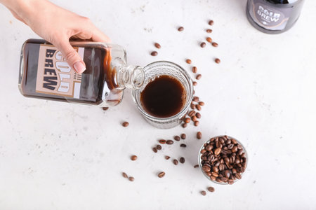 Woman pouring tasty cold brew from bottle into glass on light background