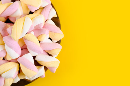 Board with tasty twisted marshmallows on yellow background