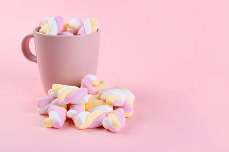Cup with tasty twisted marshmallows on pink backgroundの写真素材