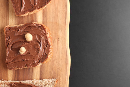 Wooden board of toasts with hazelnut butter on dark background, closeup