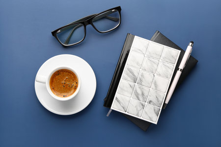 Notebooks, pen, eyeglasses and cup of coffee on blue backgroundの写真素材