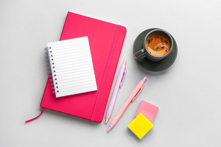 Notebooks, pens, sticky notes and cup of coffee on light backgroundの写真素材