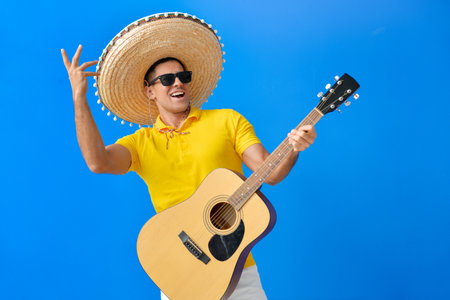 Handsome young man in sombrero hat and with guitar on color background