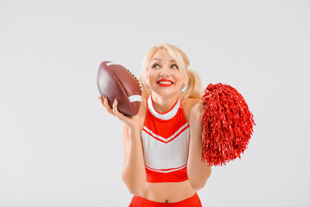 Beautiful cheerleader with rugby ball on light background