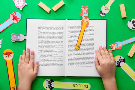 Little child with cute bookmarks reading book on color background