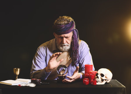 Male fortune teller with crystal ball at table on dark backgroundの写真素材