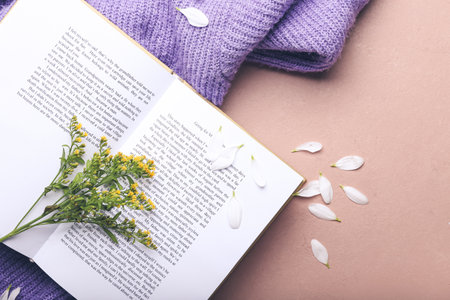 Book with fresh flowers and sweater on color background