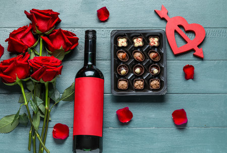 Bottle of wine, box with candies, heart and rose flowers on gray wooden background. Valentine's Day celebrationの写真素材