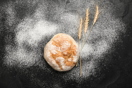 Loaf of fresh bread, wheat ears and flour on black tableの写真素材