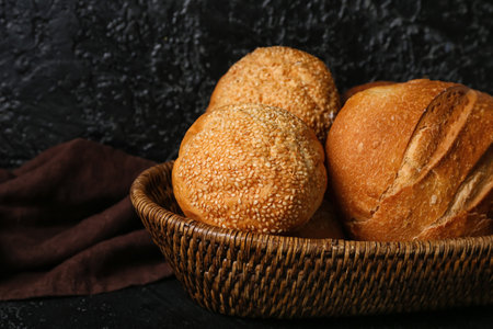 Wicker basket with loaves of different bread on black table