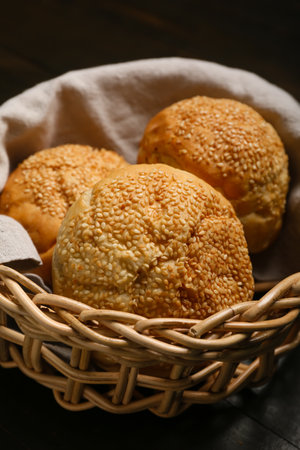 Delicious buns with sesame seeds in wicker basket on black wooden backgroundの写真素材