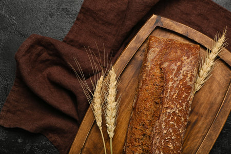 Board with loaf of fresh rye bread and wheat ears on black backgroundの写真素材