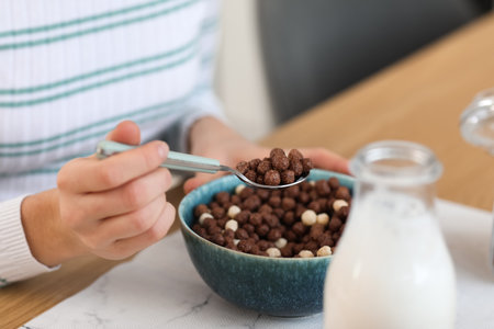 Young woman eating corn balls with spoon at table in kitchen, closeupの写真素材