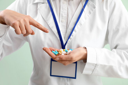 Female doctor pointing at pile of vitamin supplements on green background, closeupの写真素材