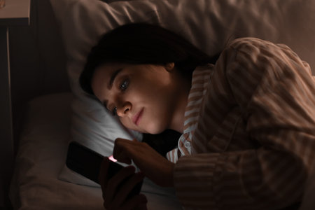 Young woman using mobile phone in bed at night, closeup