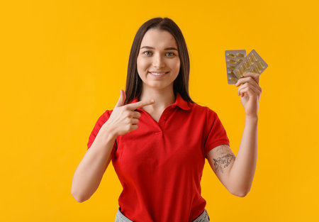 Young woman pointing at blisters of vitamin supplements on yellow backgroundの写真素材