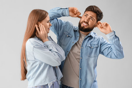 Young couple suffering from loud noise on gray backgroundの写真素材