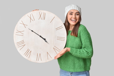 Beautiful young woman with clock on gray background