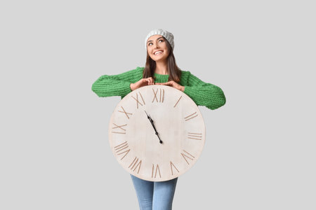 Beautiful young woman with clock on gray backgroundの写真素材