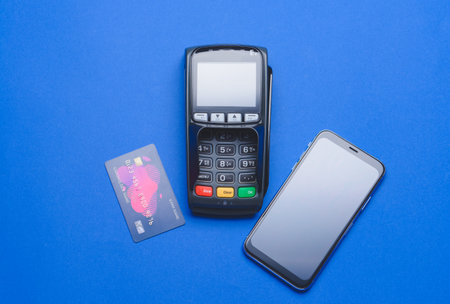Payment terminal with credit card and mobile phone on color background