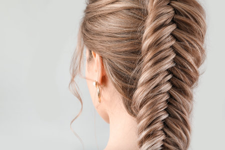 Beautiful young woman with braided hair on gray background, closeup