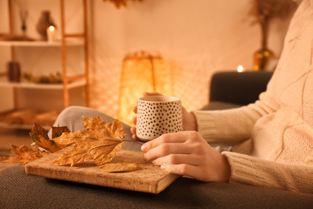 Woman with cup of coffee, book and autumn leaves at homeの写真素材