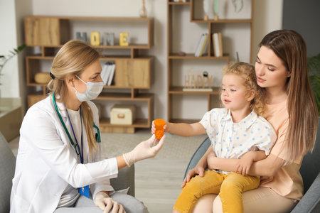 Pediatrician giving medicine to little girl at homeの写真素材