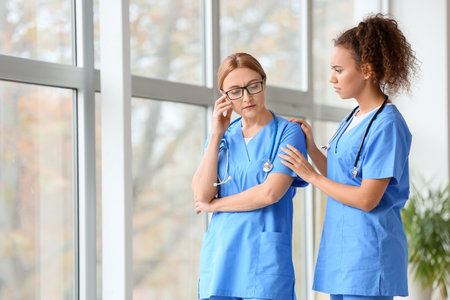 Female doctor calming her colleague in clinicの写真素材