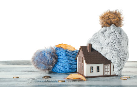 Figure of house, autumn leaves, coins and warm hats on table against white background. Concept of heating seasonの写真素材