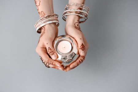 Beautiful female hands with henna tattoo and candle on gray backgroundの写真素材