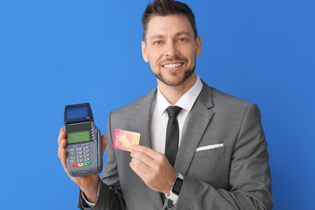 Businessman with payment terminal and credit card on color background
