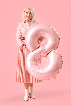 Beautiful mature woman with balloon in shape of figure 8 on pink background. International Women's...
