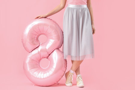 Young woman with balloon in shape of figure 8 on pink background. International Women's Day