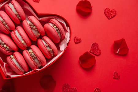 Box with tasty macaroons, hearts and rose petals on red background. Valentine's Day celebrationの写真素材