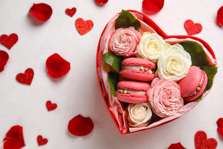 Box with tasty macaroons, rose flowers and hearts on white background. Valentine's Day celebration