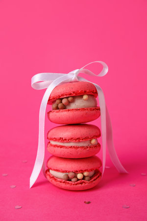 Tasty macaroons with white ribbon on pink background. Valentine's Day celebrationの写真素材