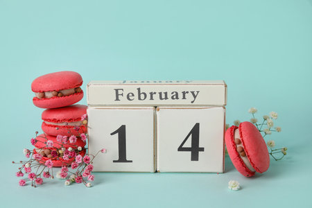 Tasty macaroons, gypsophila flowers and cube calendar with date 14 FEBRUARY on blue background. Valentine's Day celebrationの写真素材