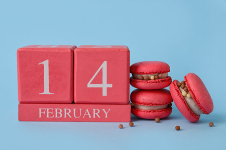 Tasty macaroons and cube calendar with date 14 FEBRUARY on blue background. Valentine's Day...