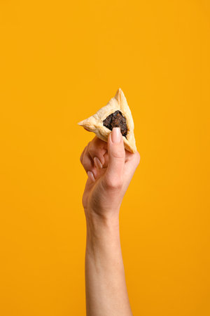 Woman with Hamantaschen cookie for Purim holiday on orange backgroundの写真素材