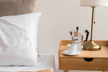 Geyser coffee maker and cup of espresso on nightstand near bedの写真素材