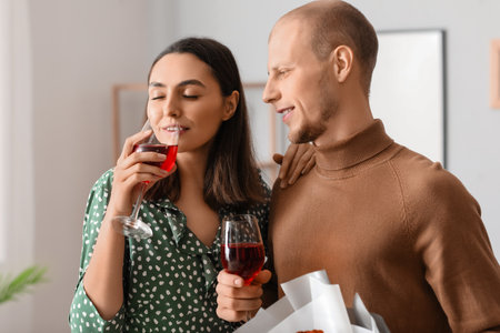 Young couple with bouquet of flowers drinking wine at home on Valentine's Dayの写真素材