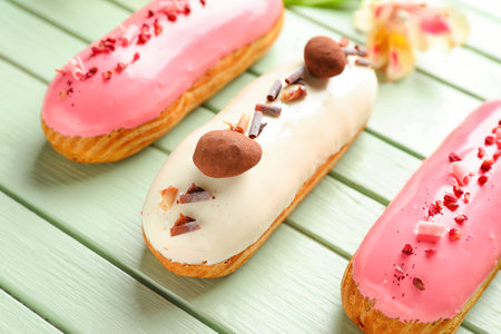 Delicious eclairs and beautiful flowers on green wooden background, closeup