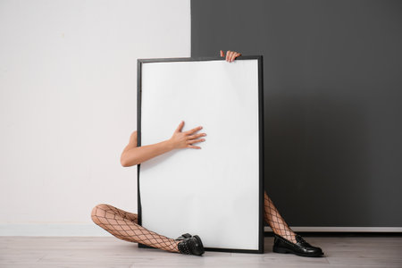 Woman in fishnet tights with blank frame sitting near black and white wallの写真素材