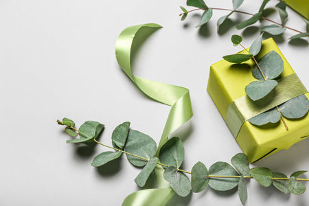 Beautiful gift box, eucalyptus branches and ribbon on light background. Women's Day celebrationの写真素材
