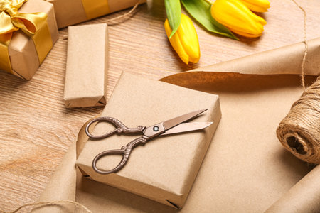 Gift boxes, wrapping paper, scissors and tulip flowers on wooden background, closeup. Women's Day...